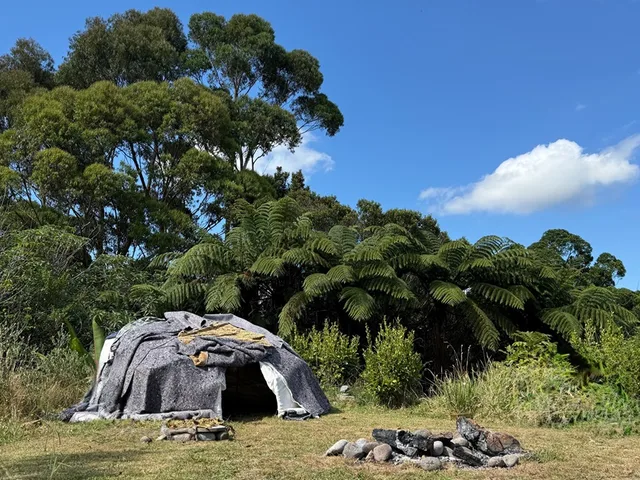 Sweat lodge and stone circle in a garden surrounded by tree ferns