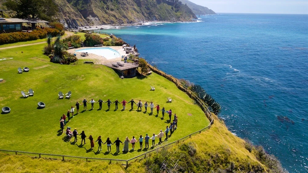 People standing in a circle on the coastal lawn at Esalen